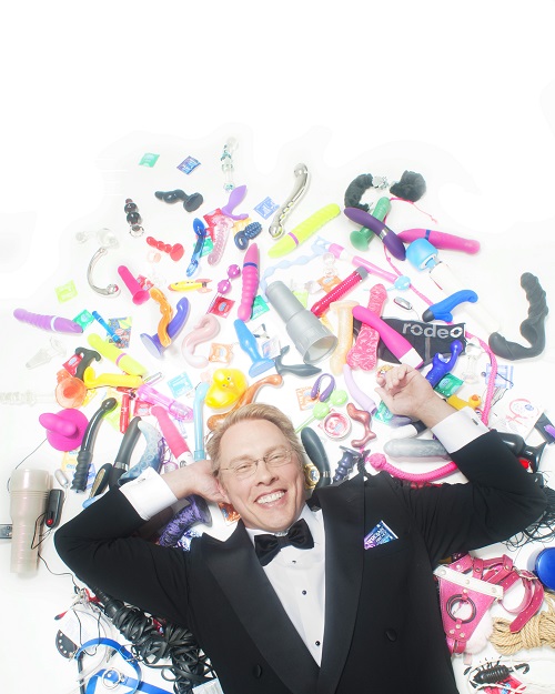 Reid Mihalko lying down, wearing a tux, surrounded by colorful sex toys