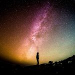 Man standing outside at night surrounded by the Milky Way sky