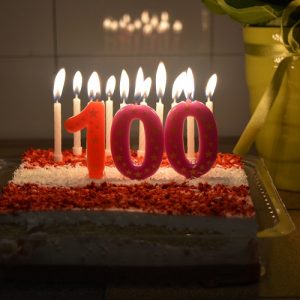 birthday cake with candles lit and "100" in front