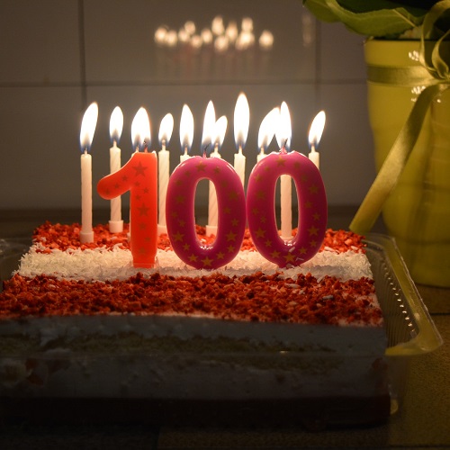 birthday cake with candles lit and "100" in front