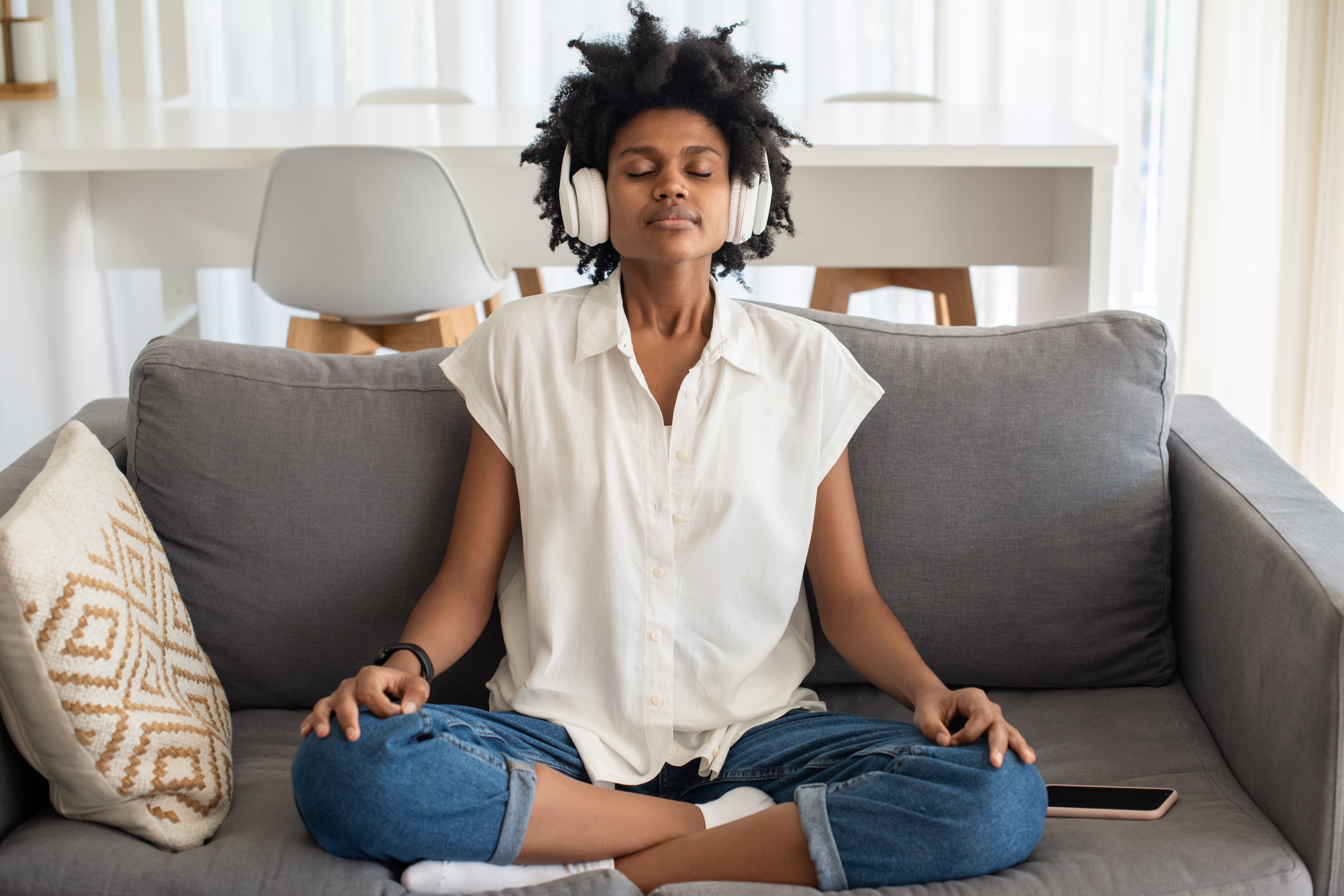 Peaceful woman sitting on sofa, meditating in headphones